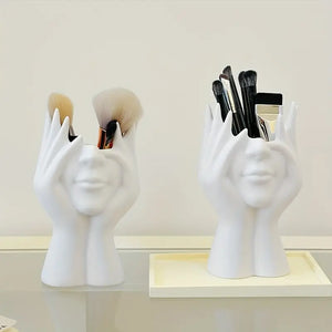 White ceramic holders shaped like hands with makeup brushes on a light background