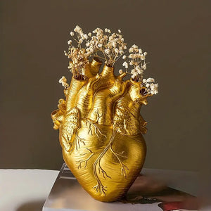 Gold heart-shaped vase with floral arrangement on a white surface against a dark background