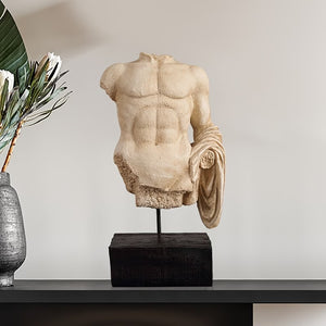 Statue of a muscular torso on a wooden base next to a vase with greenery