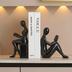 Black sculpture of a person reading a book on a white platform with 'Vogue' magazine in the background.