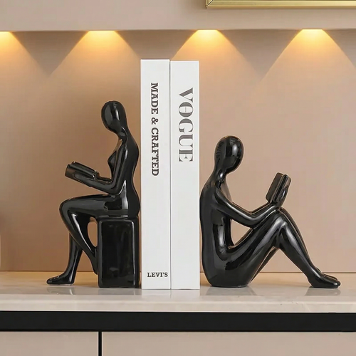 Black sculpture of a person reading a book on a white platform with 'Vogue' magazine in the background.