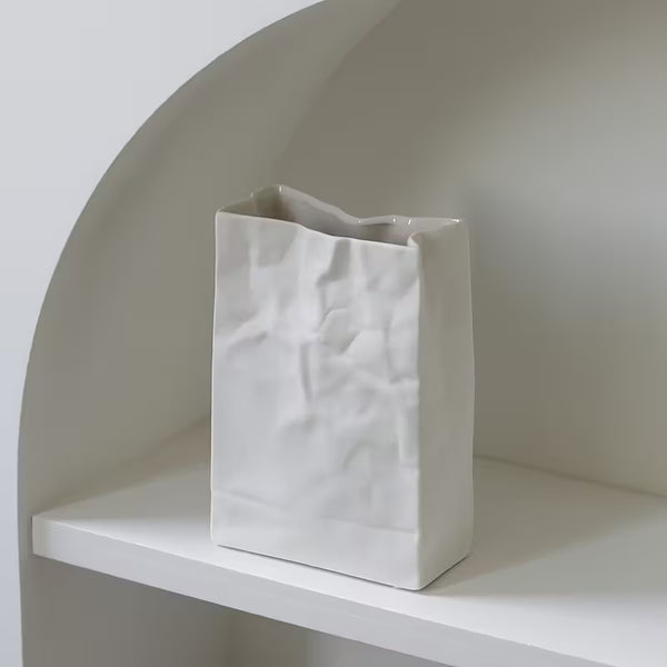 White textured vase on a white shelf against a neutral wall