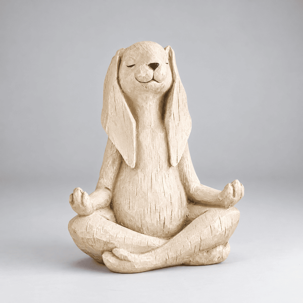 A beige textured resin figurine of a rabbit sitting cross-legged in a meditative pose, photographed against a neutral gray studio background.