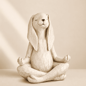 A textured ceramic rabbit figurine sitting cross-legged in a meditative yoga pose, shown against a warm beige background with soft diagonal light rays.