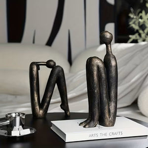 Bronze sculptures of abstract figures on a table with a book titled 'Arts The Crafts' in the background.