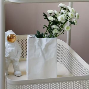 White vase with greenery and a small white figure in an astronaut suit on a perforated surface.