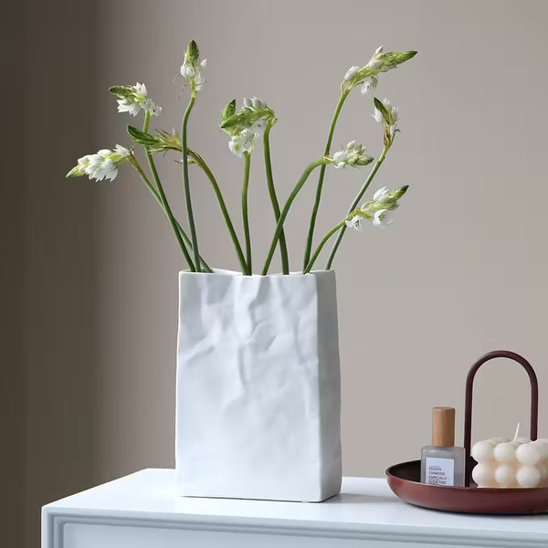 White textured vase with flowers on a white surface against a beige wall