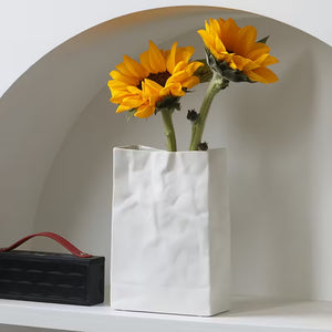 White vase with sunflowers on a shelf next to a black speaker