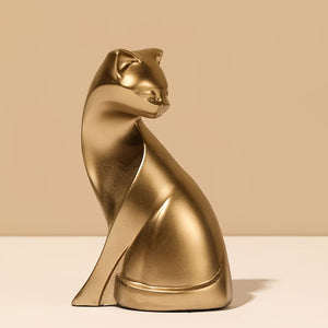 A modern, sculptural cat figurine in a glossy metallic gold finish, shown sitting on a white surface against a warm beige background.