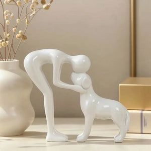 White ceramic sculpture of two abstract figures on a shelf with decorative items.